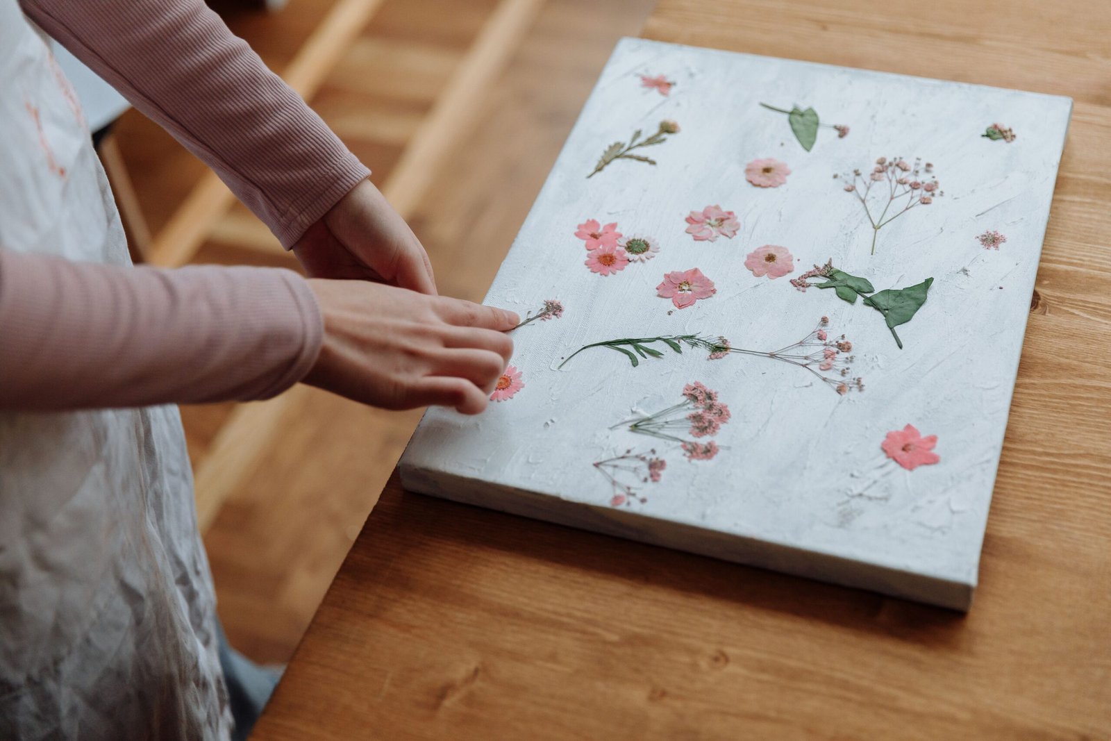 Hands arranging pressed flowers on a canvas indoors, highlighting a creative process.