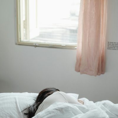 A woman peacefully sleeping in a sunlit bedroom with soft bedding and curtains.